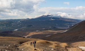 Group of hikers trekking through rugged mountainous terrain under a cloudy sky.